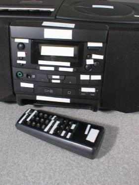 An image of a stereo and remote control with white tape over all of the buttons and printed labels.