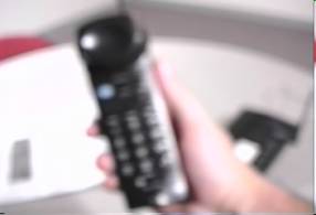 A photo of a telephone handset in an individual's hands simulates low vision. The image is significantly blurred. Text labels are unreadable and buttons are indistinguishable.